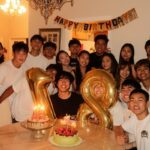 Group of young adults celebrating a birthday with cakes and gold number 18 balloons.