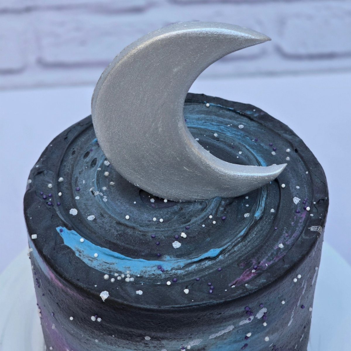 Space themed cake with dark swirled frosting and a silver crescent moon topper.
