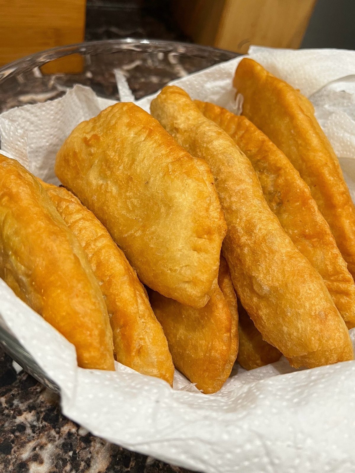 Golden-brown fried aloo potato pies piled in a paper-lined metal bowl.