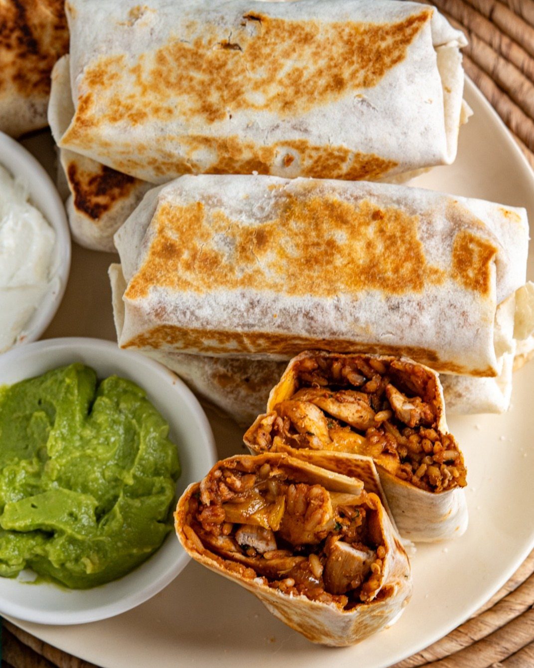 Toasted chicken and rice burritos on a plate with guacamole and sour cream.