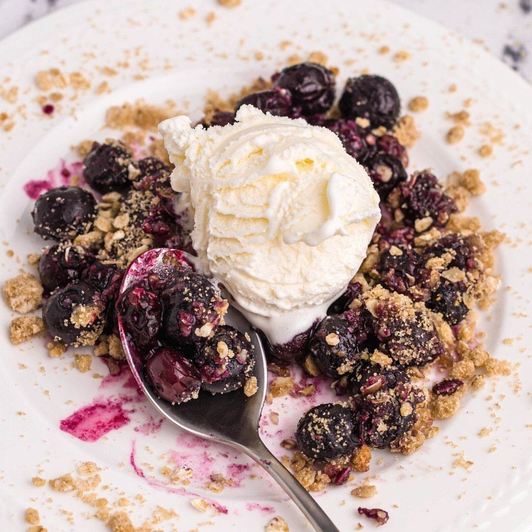 Blueberry crumble with a scoop of vanilla ice cream on a white plate.