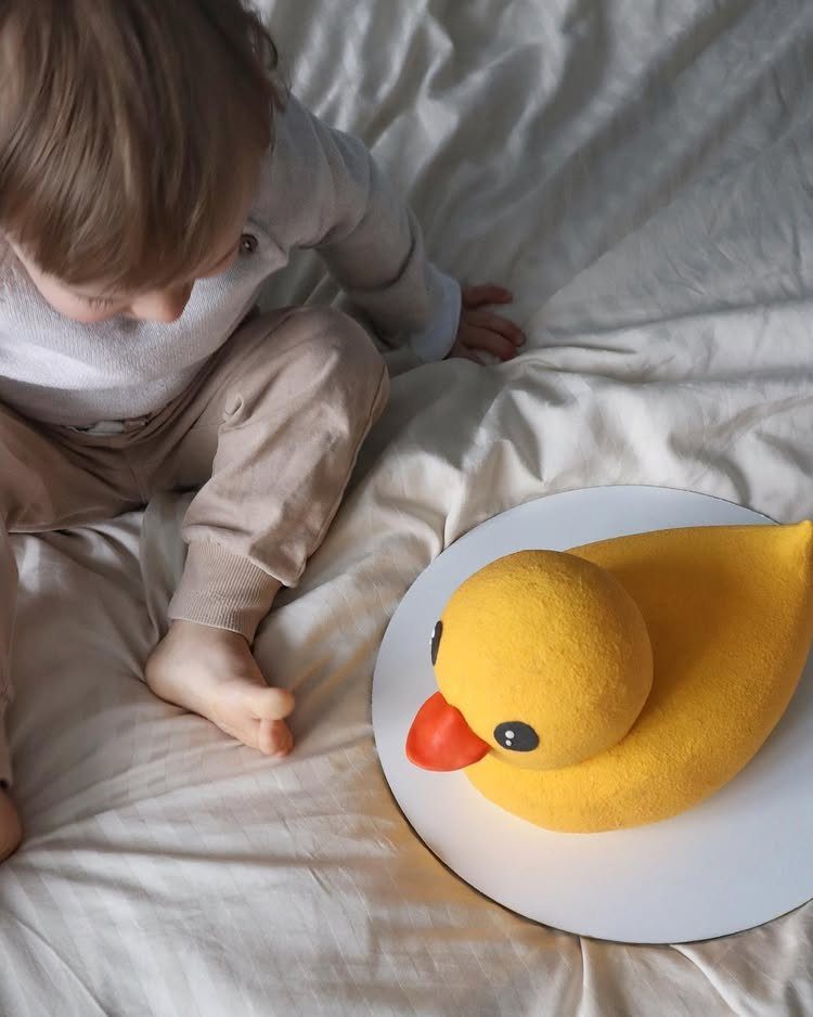 Yellow duck-shaped cake on a white plate with a child looking on.