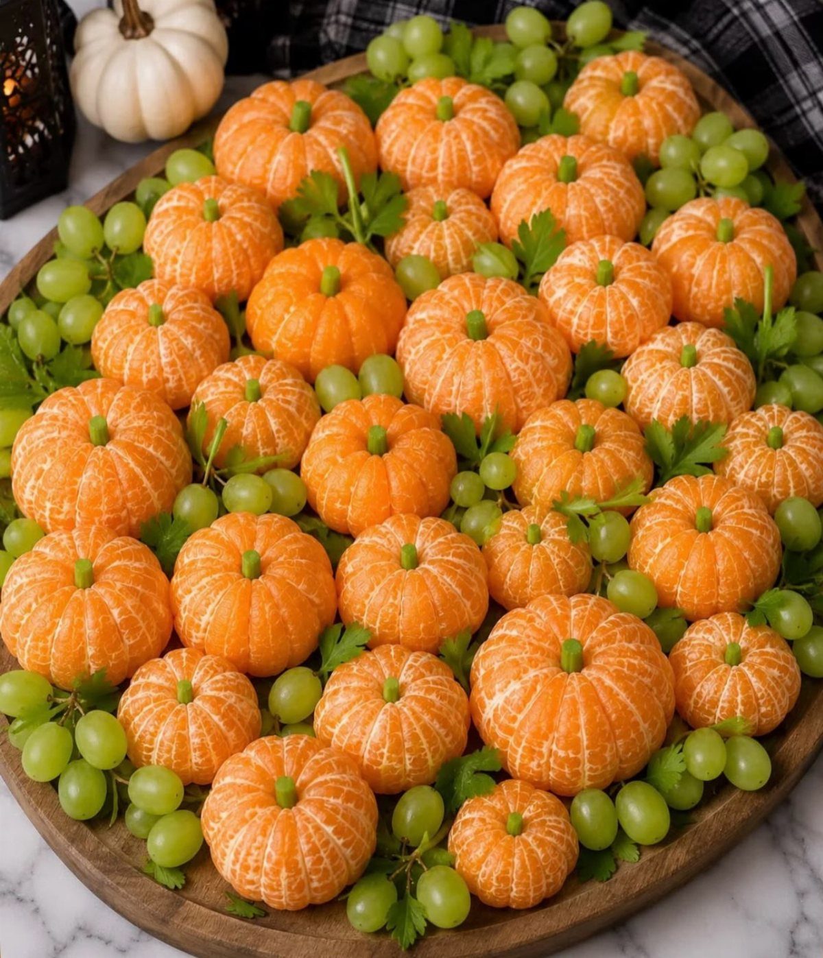 Carved clementine pumpkins and green grapes arranged on a round wooden serving platter.
