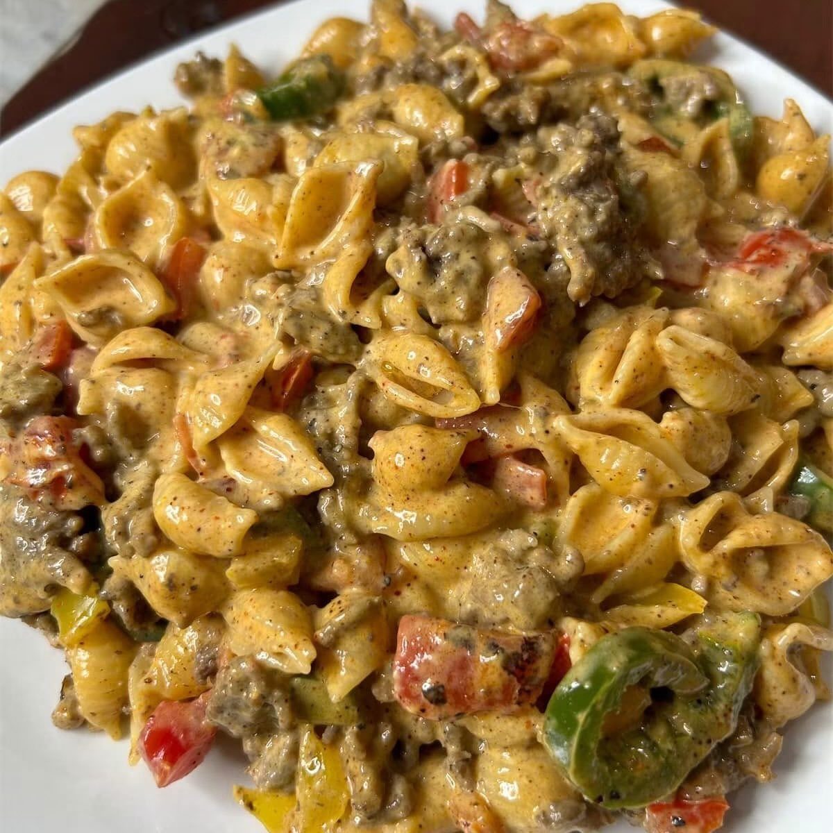 Shell pasta with ground meat, creamy sauce, and colorful bell peppers on a plate