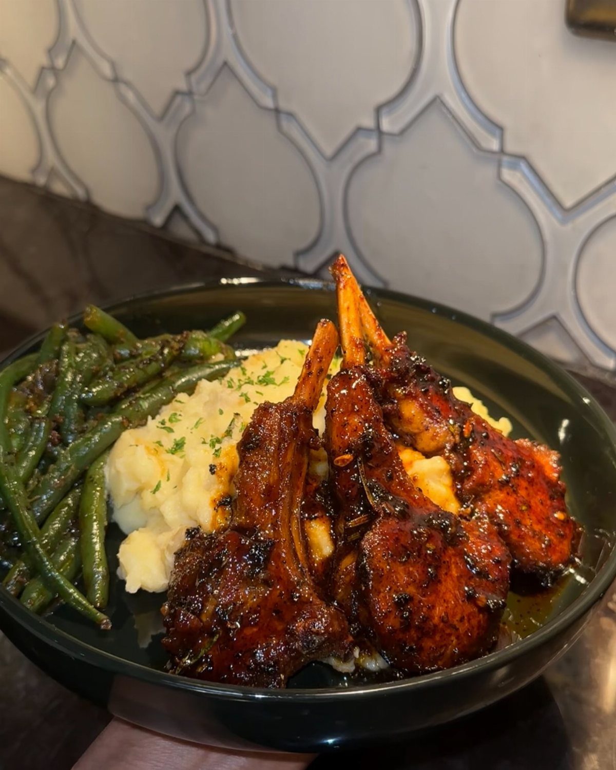 Glazed lamb chops with mashed potatoes and green beans on a black plate