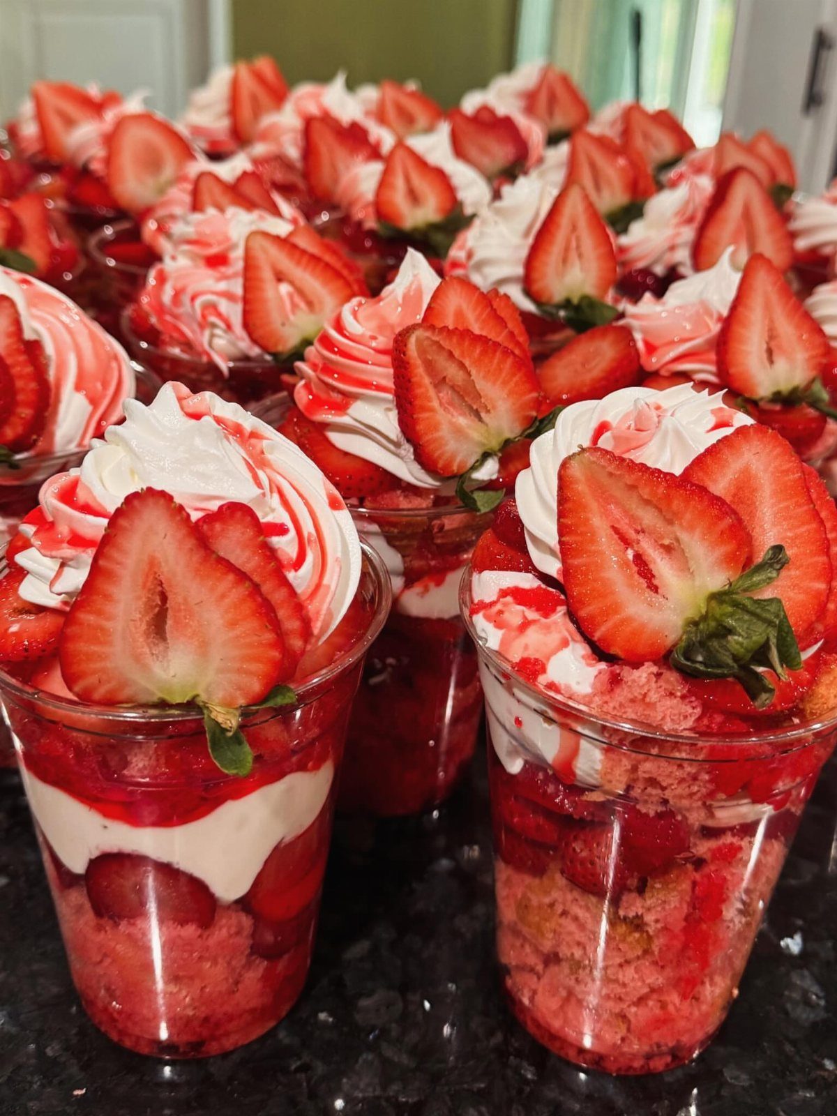 Strawberry crumble desserts in plastic cups topped with whipped cream and fresh strawberries