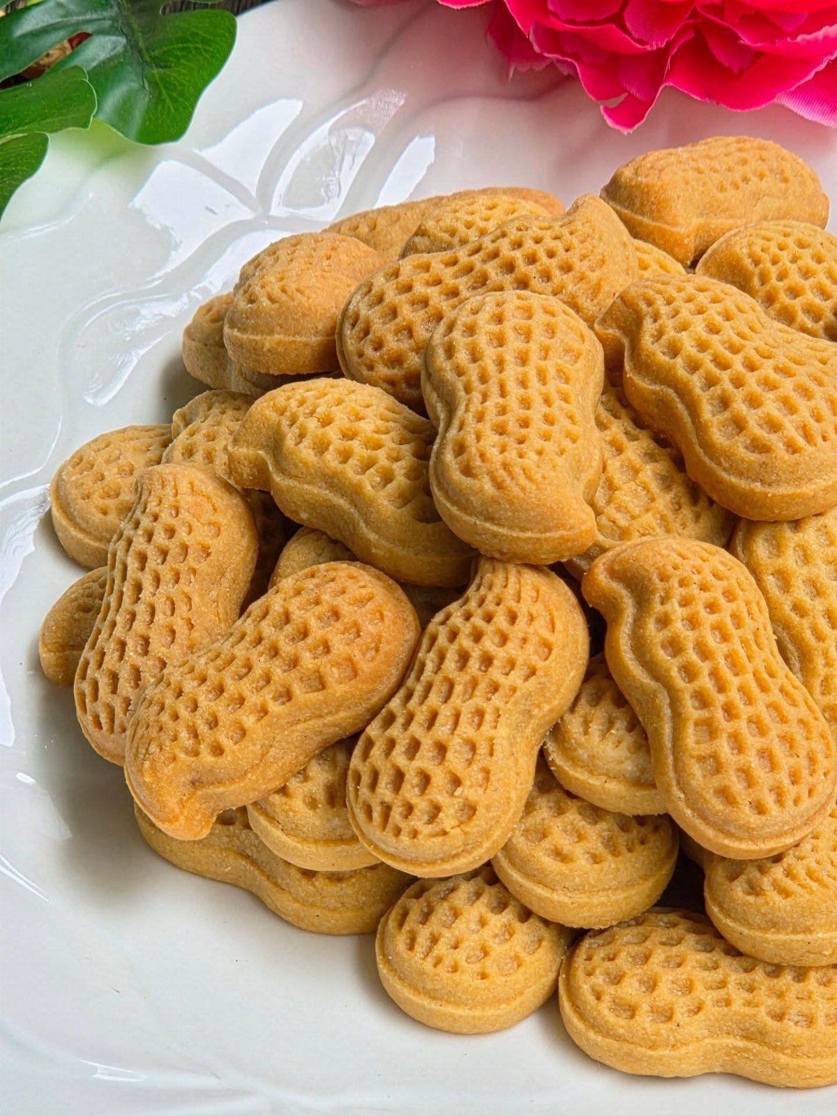 Peanut shaped golden-brown cookies piled on a white decorative ceramic plate.