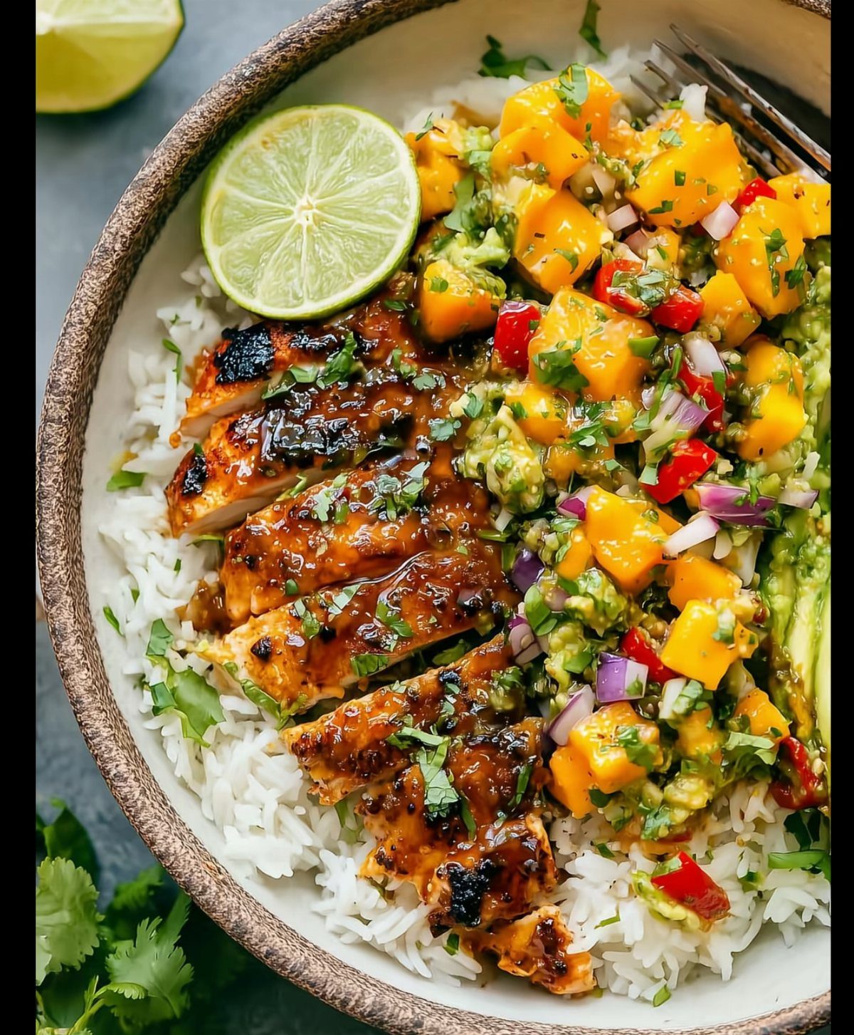 Grilled glazed chicken and mango salsa served over white rice in a bowl.