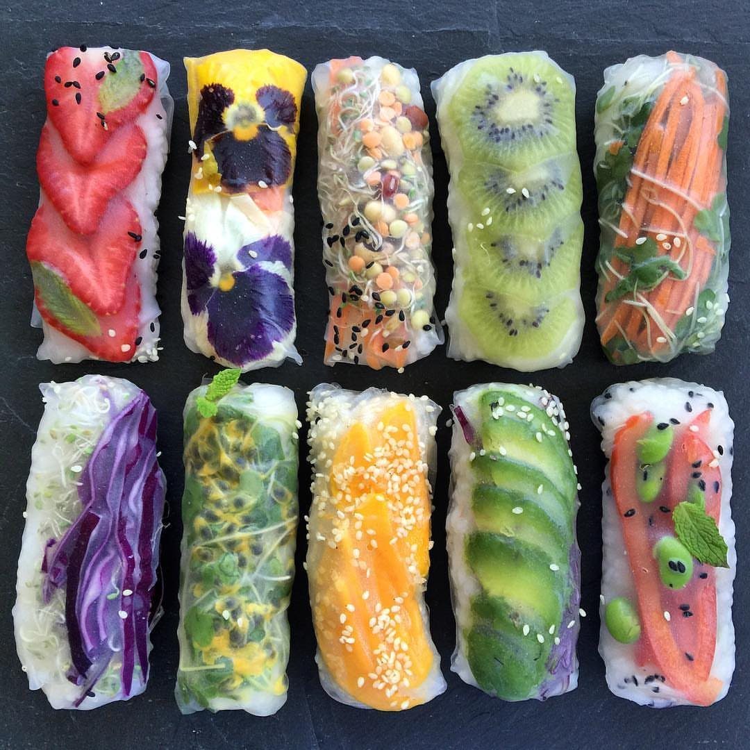 Colorful fruit and vegetable spring rolls wrapped in translucent rice paper on slate.