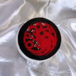 Round black cake with a red three-headed dragon emblem on silver satin fabric.