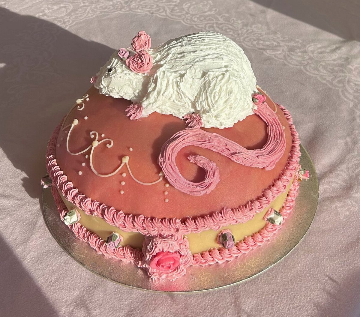 Pink birthday cake topped with a white frosting rat with pink ears and tail.