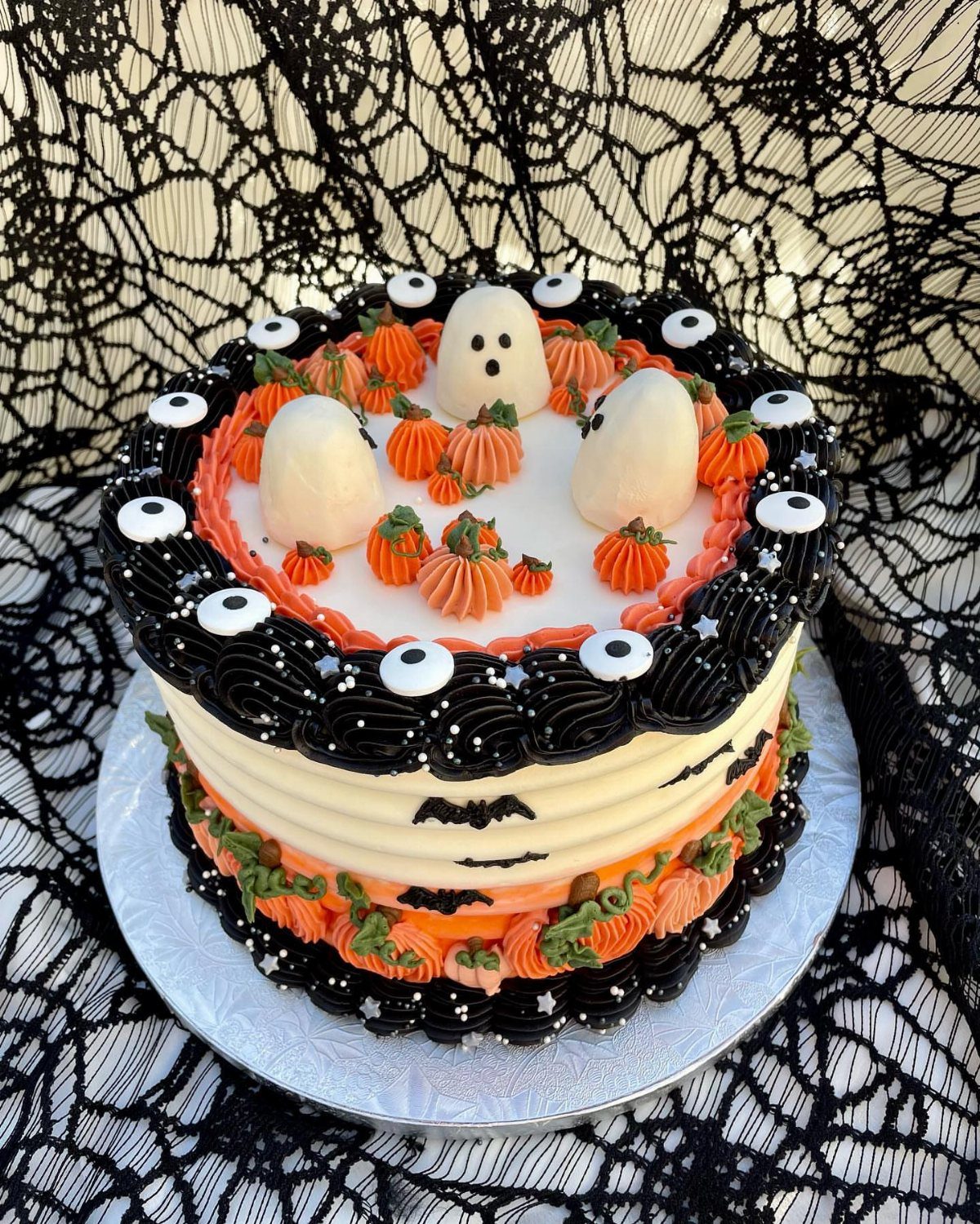 Halloween cake with orange pumpkins, white ghosts, and eyeballs on a spiderweb background