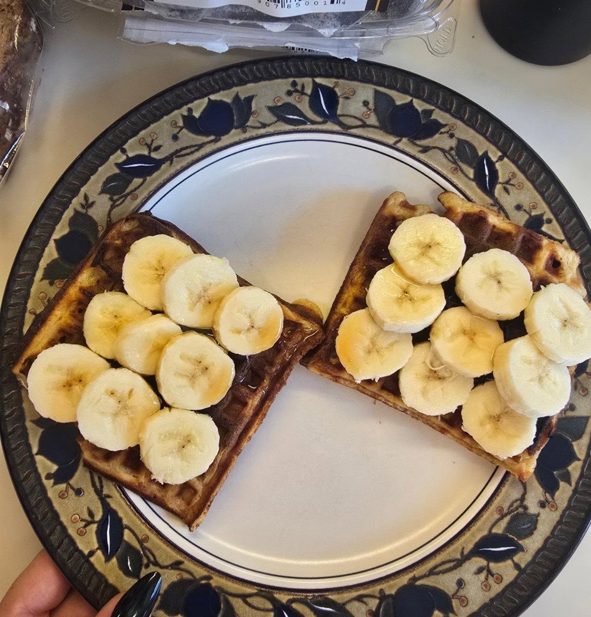 Two toasted waffles topped with fresh banana slices on a blue floral plate.